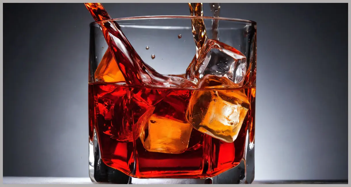 An abstract close-up of Negroni punch liquid, showing light refraction through ice with intense ruby red and amber tones against a dark background.