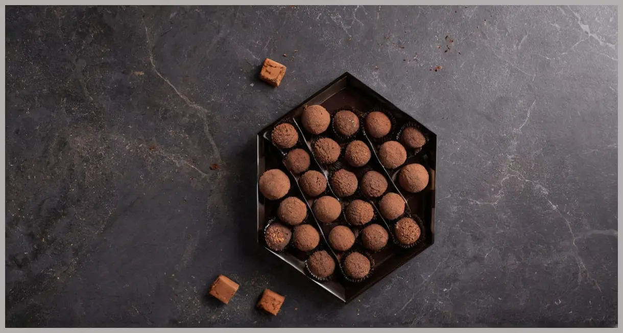 Overhead flat lay of vegan chocolate truffles on dark marble, surrounded by cocoa and chocolate pieces. Paul A Young’s vegan chocolate truffles