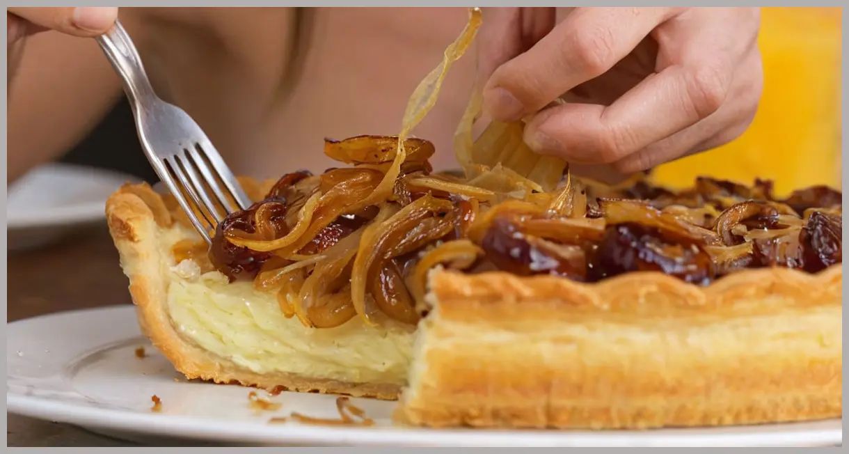 Extreme close-up of a fork lifting vegan tart, backlit golden warmth, stretching miso onions. Vegan tart with miso, frangipane and onions