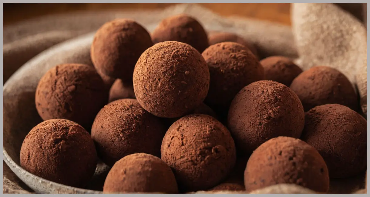 Ultra-detailed close-up of glossy vegan chocolate truffles dusted with cocoa powder, bathed in golden hour light. Paul A Young’s vegan chocolate truffles