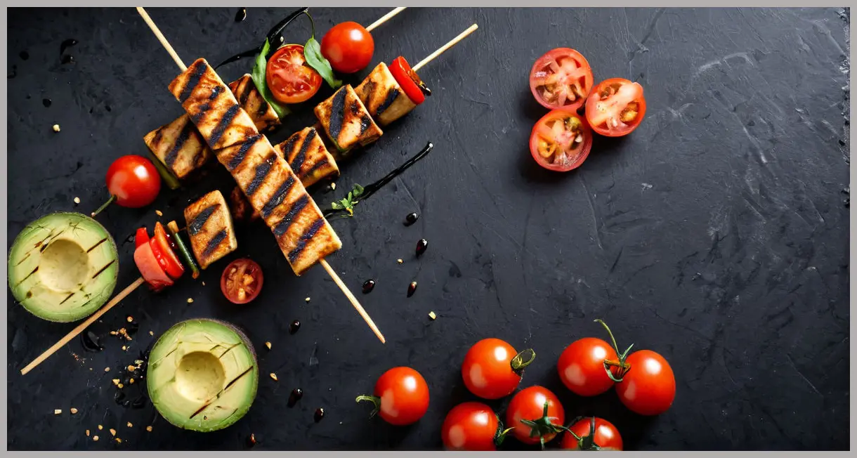 Dutch angle of grilled smoky chipotle tofu skewers with avocado and tomatoes, charred marks, and rising smoke. Smoky chipotle tofu with tomatoes and avocado