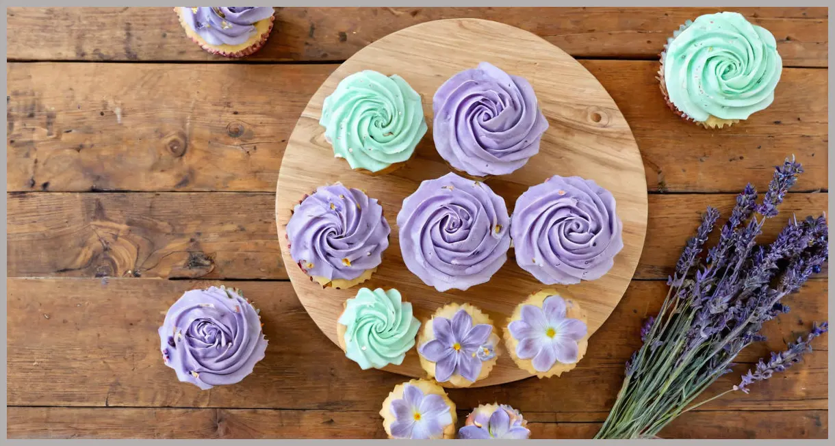 Overhead view of lavender cupcakes arranged in a circle on a wooden table, with pastel frosting and scattered lavender buds.