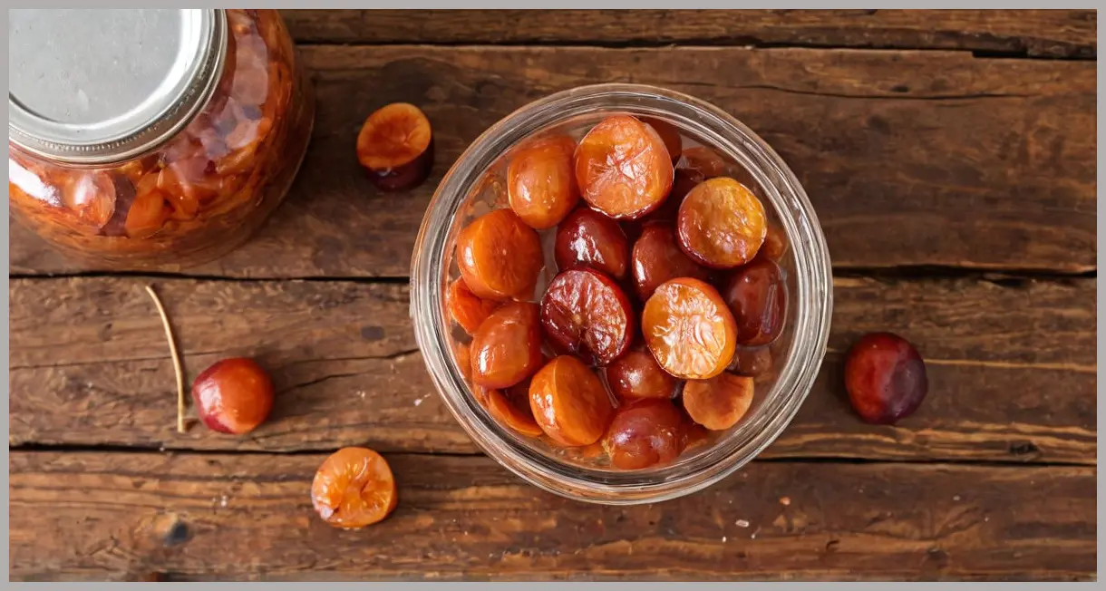 Overhead view of a glass jar filled with layered British plum umeboshi, salt flakes glistening in golden hour light. British plum umeboshi