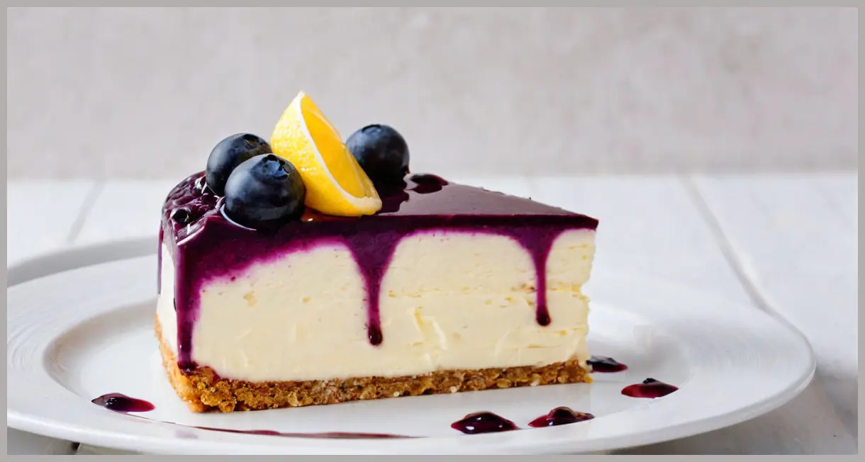 A macro shot of a single slice of frozen lemon and blueberry mousse cake on white porcelain, highlighting blueberry bursts, lemon curd swirls, and white chocolate shavings.
