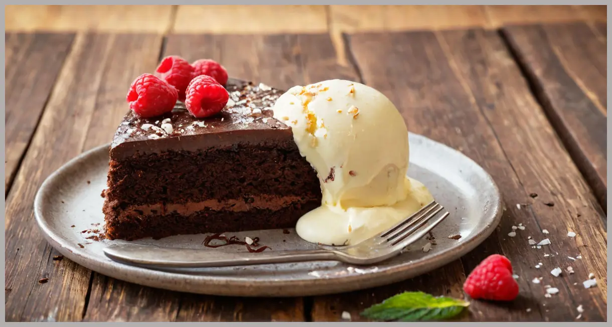 Overhead flat lay of a sliced Easy flourless chocolate cake with gooey center, vanilla ice cream melting, raspberries, and mint on a rustic wooden table in golden hour light.