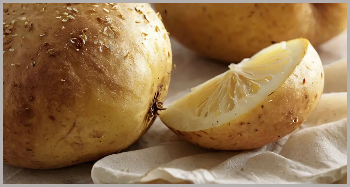 Garlic roast potatoes with bay leaves, macro shot of a split potato revealing fluffy interior, crispy skin, and clinging garlic fragments.