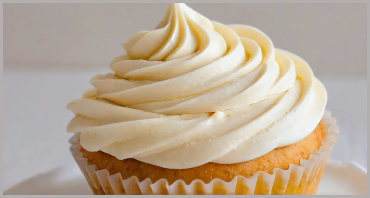 Close-up of a freshly piped swirl of creamy buttercream icing atop a vanilla cupcake, ultra-smooth texture with subtle sheen. Simple buttercream icing