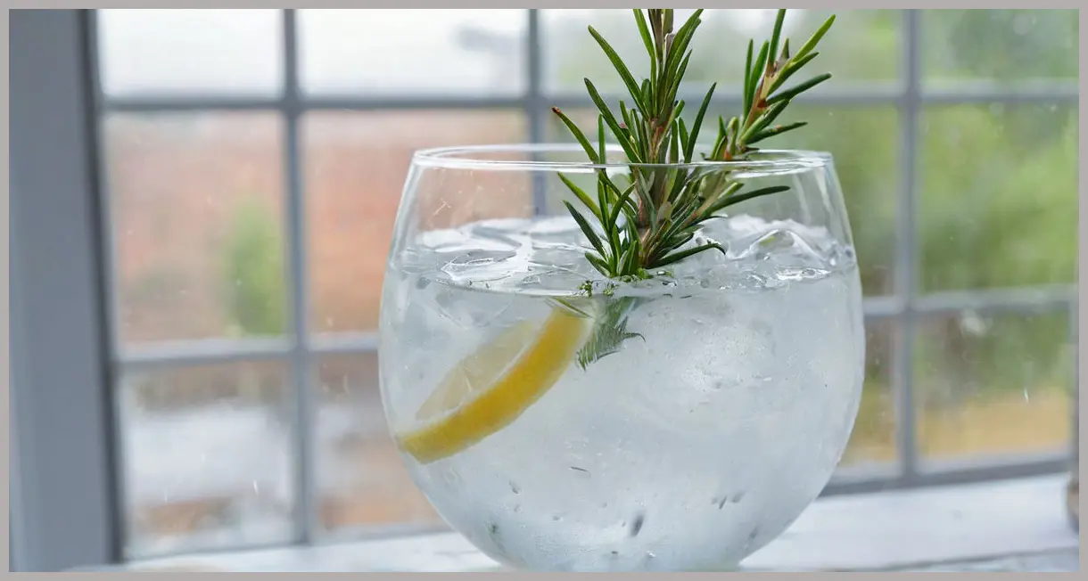 An Elderflower gin and tonic in a chilled gin balloon glass, featuring an extreme close-up of a rosemary sprig and heavy condensation on the glass.
